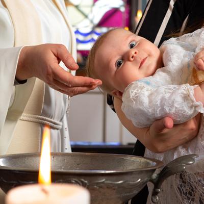 Pappi kastaa lasta. Papin käsi ilmassa kastemaljan yllä. vasemmalla etualalla palava kynttilä.